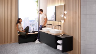 Woman sitting on windowsill in bathroom with Geberit ONE products, talking to man